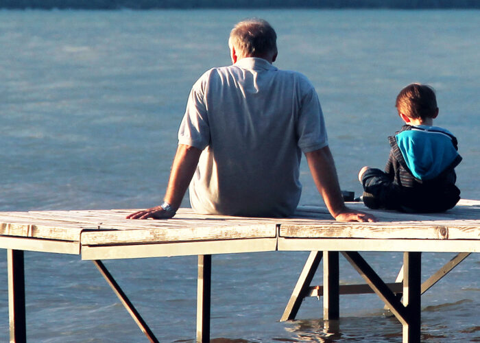 An image of a grandfather and his grandson sitting on a wooden dock at the lake